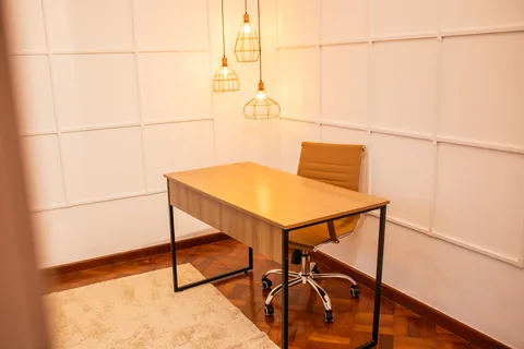 Mesa de trabalho de madeira sob pendentes aramados acesos, com paredes em boiserie branca