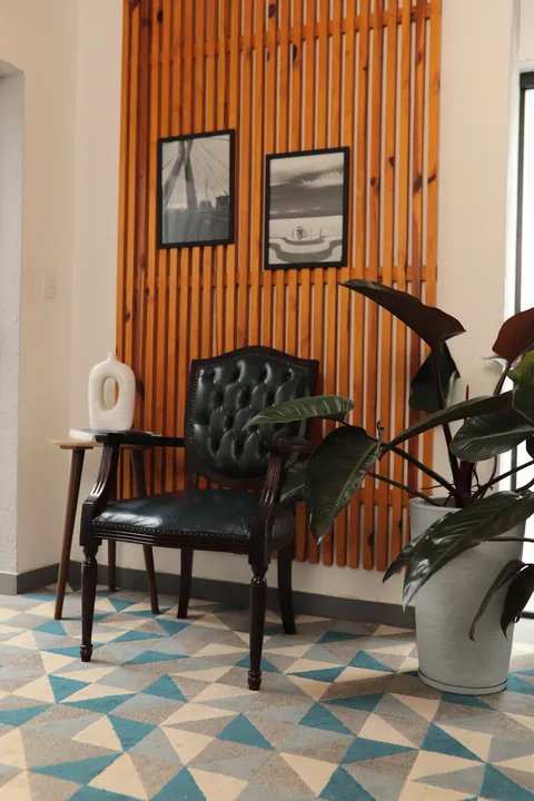 Cadeira capitonê preta diante de painel ripado de madeira com quadros, sobre tapete geométrico azul