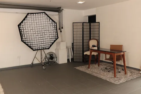 Octabox montada ao lado do biombo e da mesa de trabalho, com ventilador e banquetas brancas