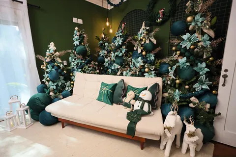 Cenário de Natal verde do Estúdio Elegance com sofá branco, almofadas de veludo, boneco de neve de pelúcia e árvores decoradas
