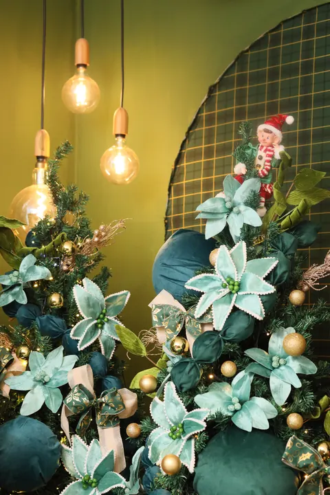 Pendentes com lâmpadas de filamento acesas sobre árvore de Natal com flores azul-turquesa e bolas douradas