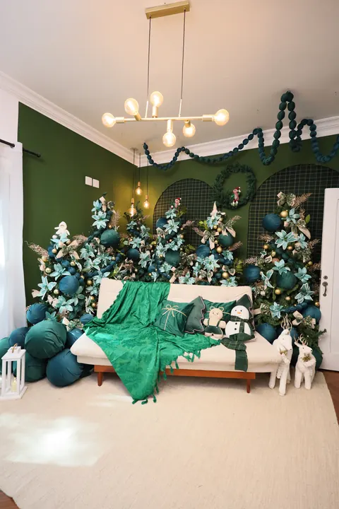 Visão geral do Estúdio Elegance no Natal: parede verde, lustre dourado, arcos xadrez e árvores em tons de esmeralda