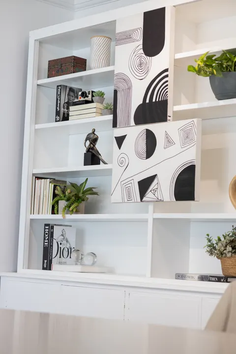 Estante branca com livros, vasos e quadros gráficos em preto e branco