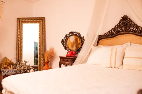 Cama clássica com dossel branco, almofadas e cabeceira entalhada em madeira escura