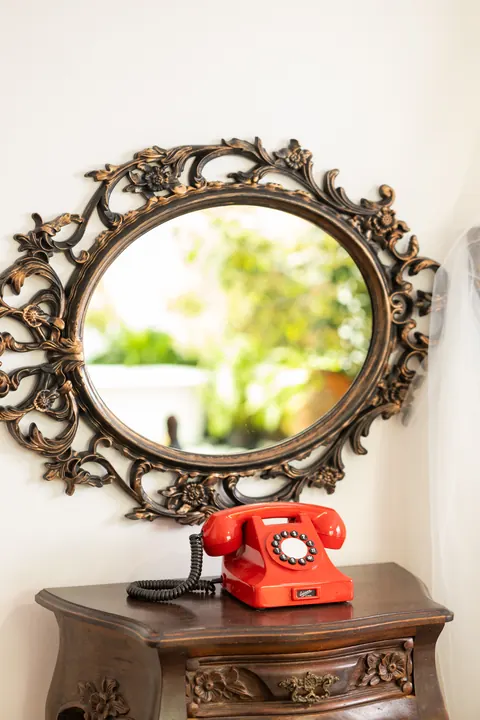 Espelho oval entalhado sobre aparador antigo com telefone vermelho