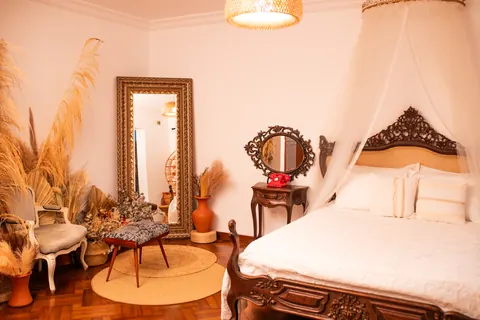 Quarto do Estúdio Majestic com cama de cabeceira entalhada, dossel, espelho dourado e plumas secas