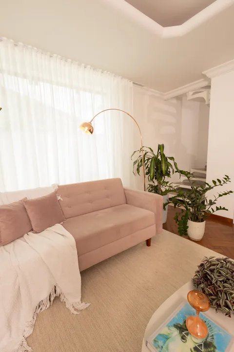 Sofá rosa com manta, luminária de arco e cortina clara com luz natural