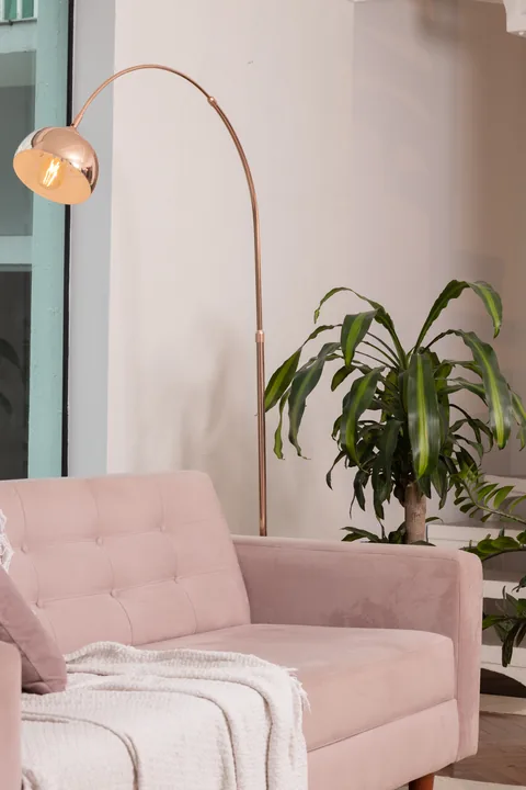 Sofá rosa com manta branca, luminária de arco dourada e planta